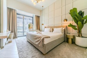 Ein modernes Hotelzimmer mit einem großen Bett, Nachttischen, einer Zimmerpflanze und Blick durch das Fenster.