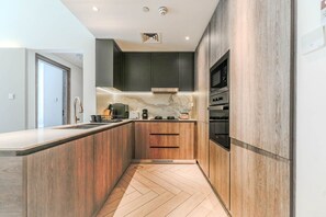 A modern kitchen with wooden cabinetry, a marble backsplash, and stainless steel appliances. - HAVN - Modern 2 Bed in Oxford 212, JVC (Dubai)