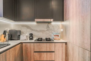 A modern kitchen with dark cabinets, a marble backsplash, and a coffee machine. - HAVN - Modern 2 Bed in Oxford 212, JVC (Dubai)