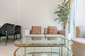 A modern living room with a glass coffee table, two patterned cushions, a grey sofa, and a black chair. - HAVN - Modern 2 Bed in Oxford 212, JVC (Dubai)