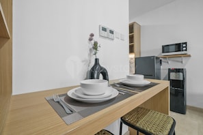 A modern kitchen with a dining table set for two, a microwave, and a refrigerator. - Harumi by Kozystay - Sudirman (Central Jakarta)