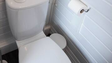 A white toilet with a paper towel holder and a toilet paper roll on the wall.