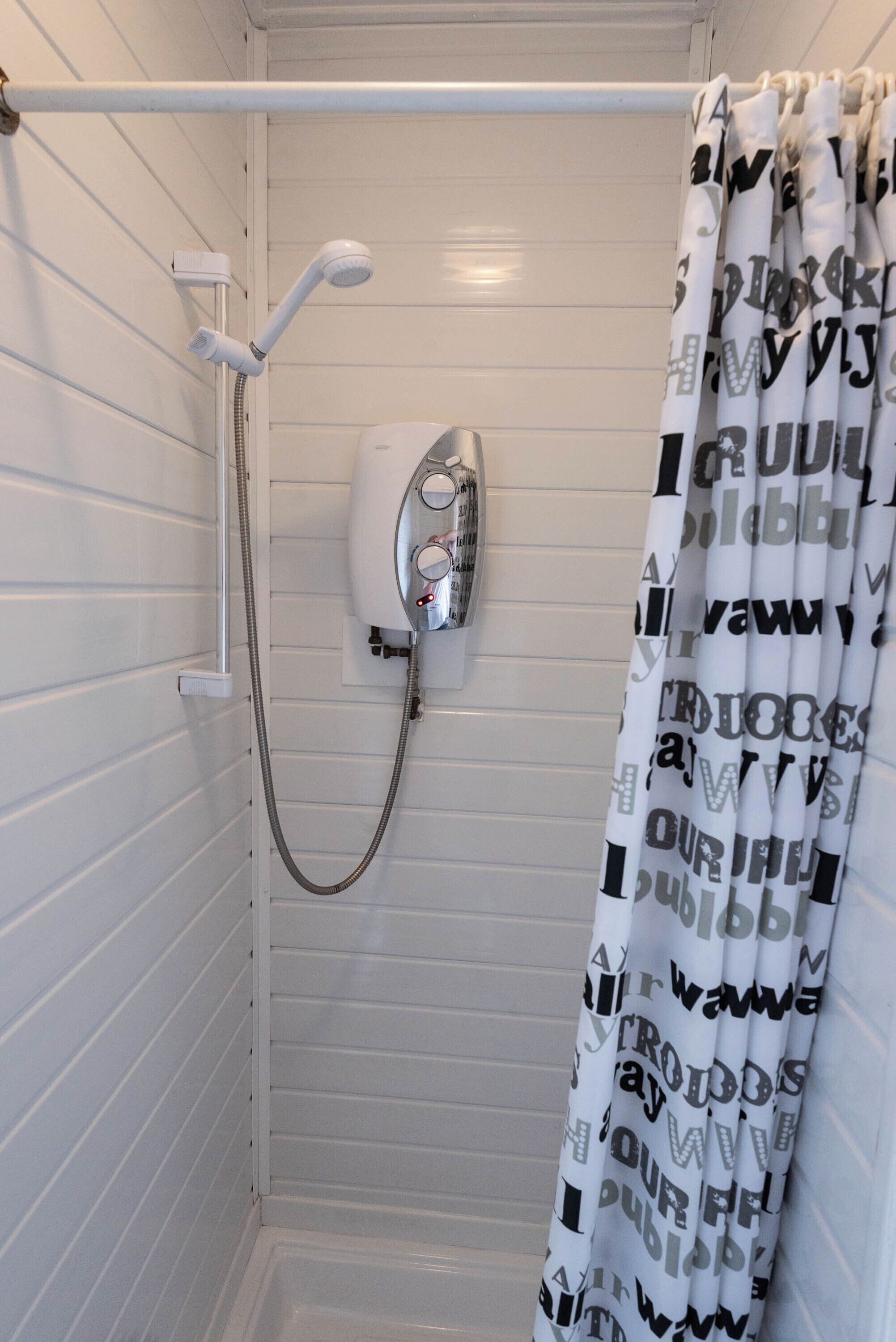 Ducha con cortina blanca, cabezal de ducha manual y panel de control en la pared.