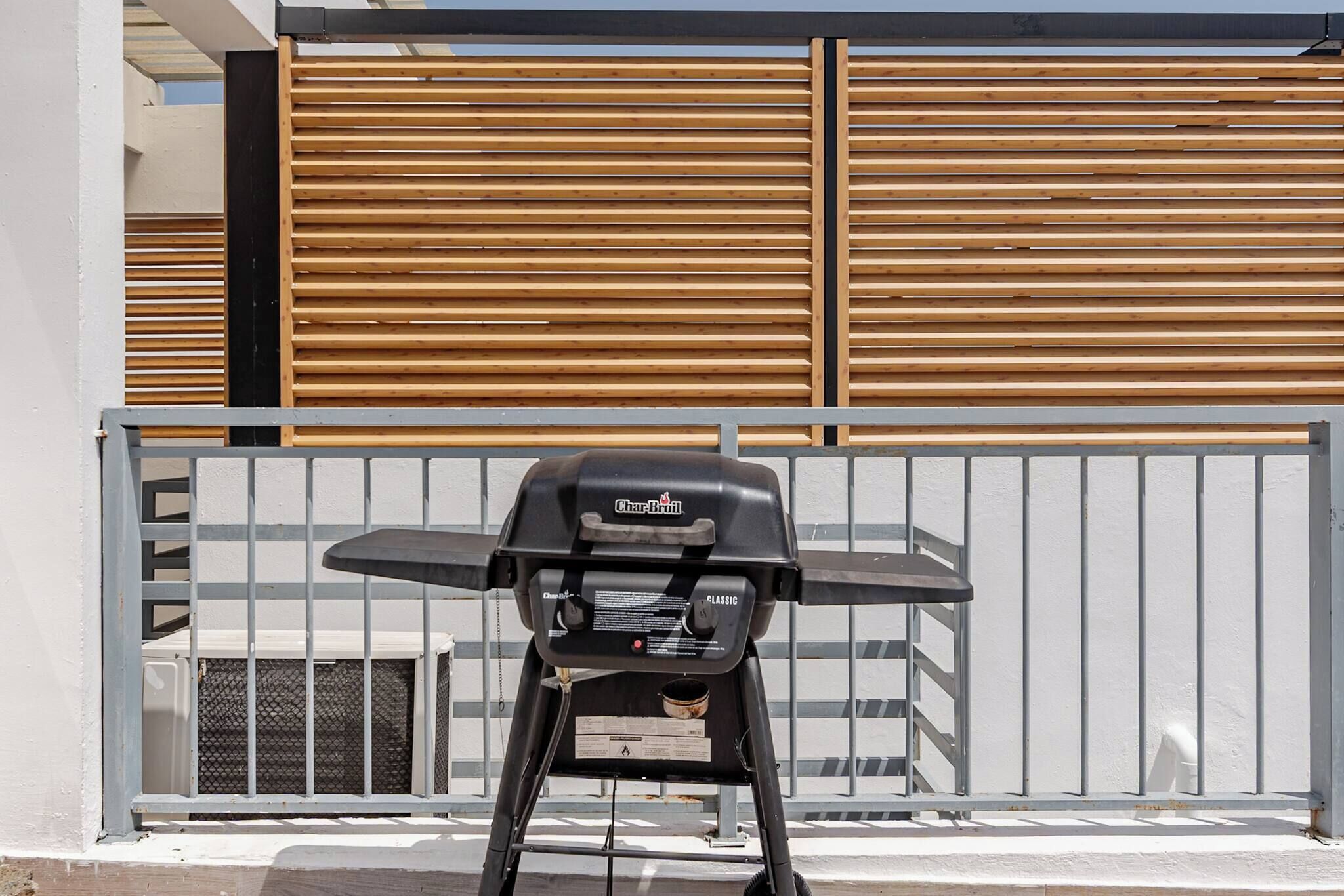 A Char-Broil Classic grill positioned in front of a white wall with a wooden slat fence.