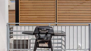 A Char-Broil Classic grill positioned in front of a white wall with a wooden slat fence.