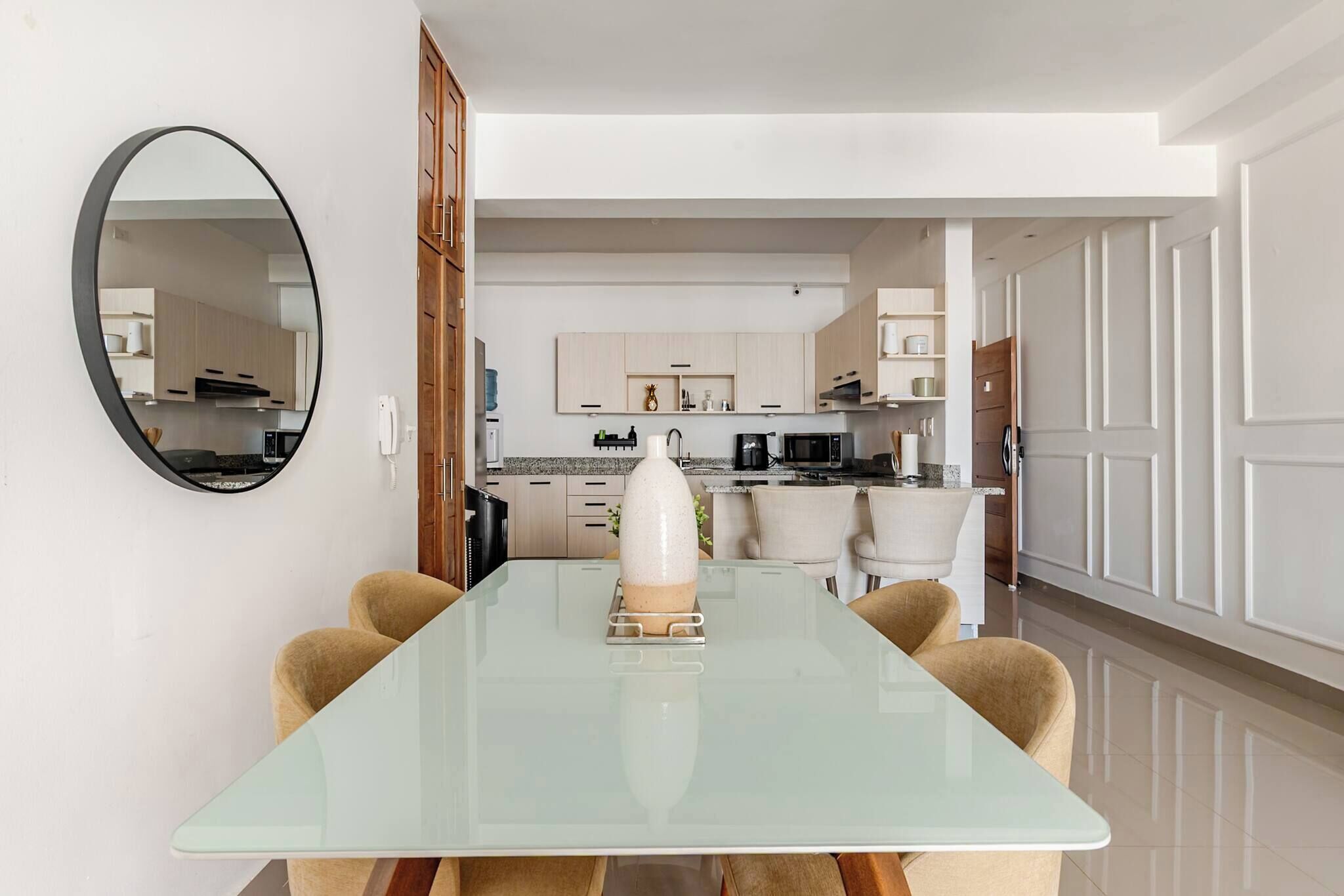 Een moderne keuken met witte kasten, een eettafel met stoelen en een grote spiegel aan de muur.