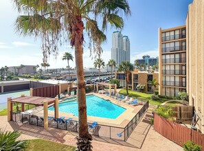 A swimming pool with lounge chairs, surrounded by a brick deck, palm trees, and modern buildings in the background. - 3B/2B Seavista Beach Front Great View (South Padre Island)