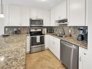 A modern kitchen with white cabinets, stainless steel appliances, granite countertops, and a granite backsplash. - 3B/2B Seavista Beach Front Great View (South Padre Island)