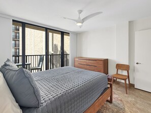 Quarto com cama, cômoda, cadeira e ventilador de teto, além de vista para o exterior.
