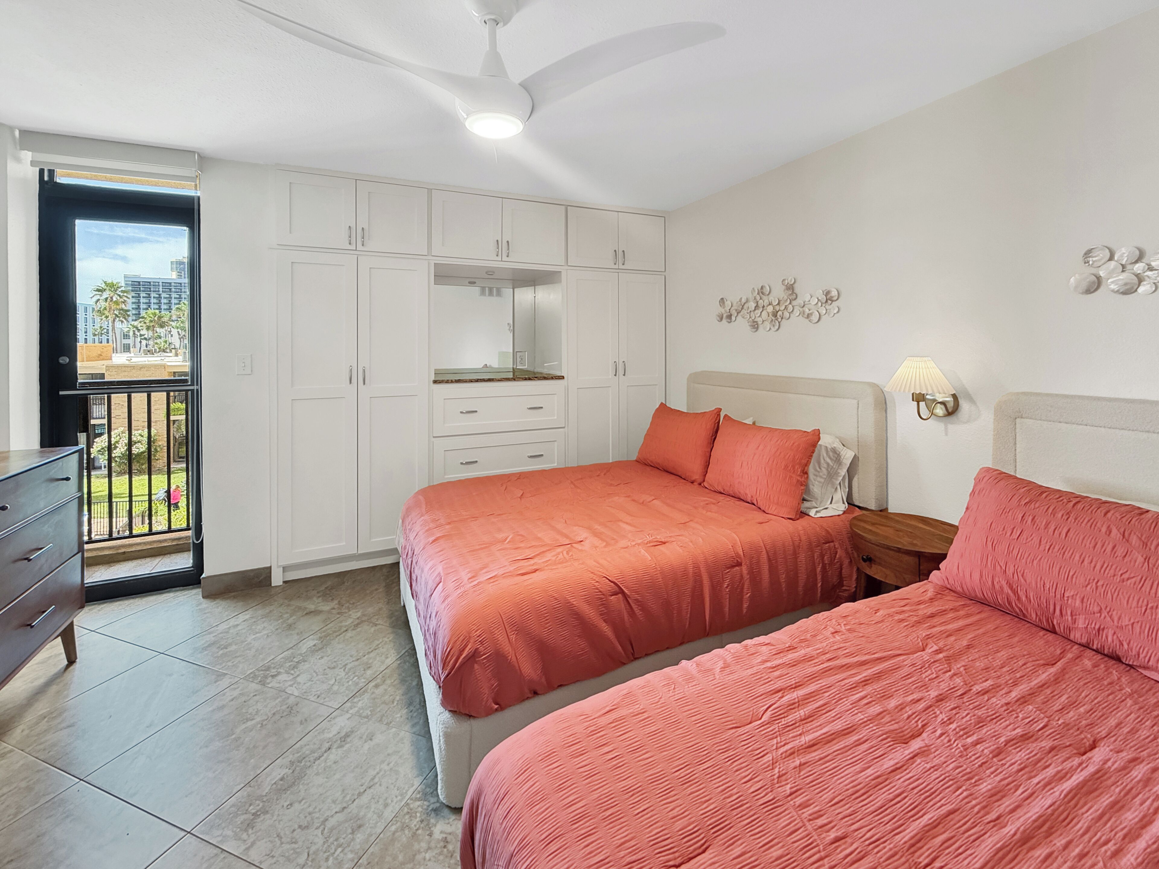 Une chambre avec deux lits, une armoire, un balcon et un ventilateur de plafond.