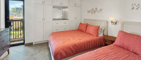 Une chambre avec deux lits, une armoire, un balcon et un ventilateur de plafond.