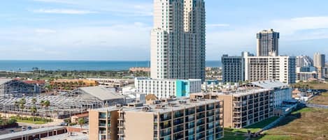 A high-rise building with multiple floors, surrounded by other buildings, and a view of the ocean in the background.