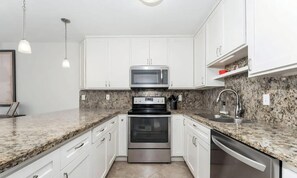 A modern kitchen with white cabinets, granite countertops, stainless steel appliances, and pendant lighting. - 3B/2B Seavista Beach Front Great View (South Padre Island)