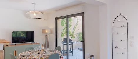 A dining area with a table set for four, a television, a lamp, and a sliding glass door leading to an outdoor patio.