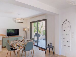A dining area with a table set for four, a television, a lamp, and a sliding glass door leading to an outdoor patio. - Les Sources by Interhome (Draguignan)