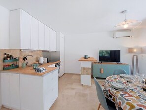 A compact kitchen with white cabinets, a wooden countertop, a dining area with a patterned tablecloth, and a television. - Les Sources by Interhome (Draguignan)
