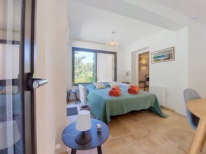 A bedroom with a bed, a table with a lamp, a chair, and a view of the outdoors. - Les Sources by Interhome (Draguignan)