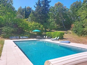 A rectangular swimming pool with clear blue water, surrounded by a paved deck. There are lounge chairs and a small table with a blue umbrella. - Les Sources by Interhome (Draguignan)