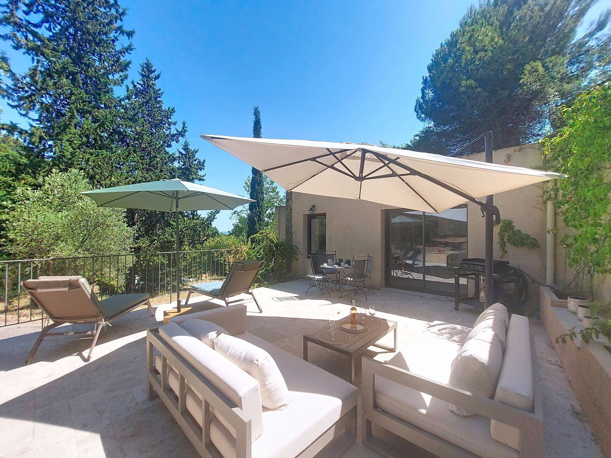 Une terrasse extérieure avec un ensemble de canapés, deux parasols et une table à manger.