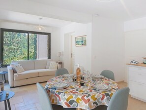 A dining area with a round table set for four, a sofa, and a window with a view of greenery. - Les Sources by Interhome (Draguignan)