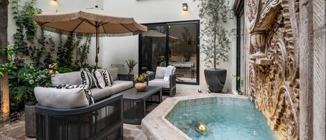 Un patio al aire libre con un sofá, una mesa, una sombrilla y un jacuzzi.