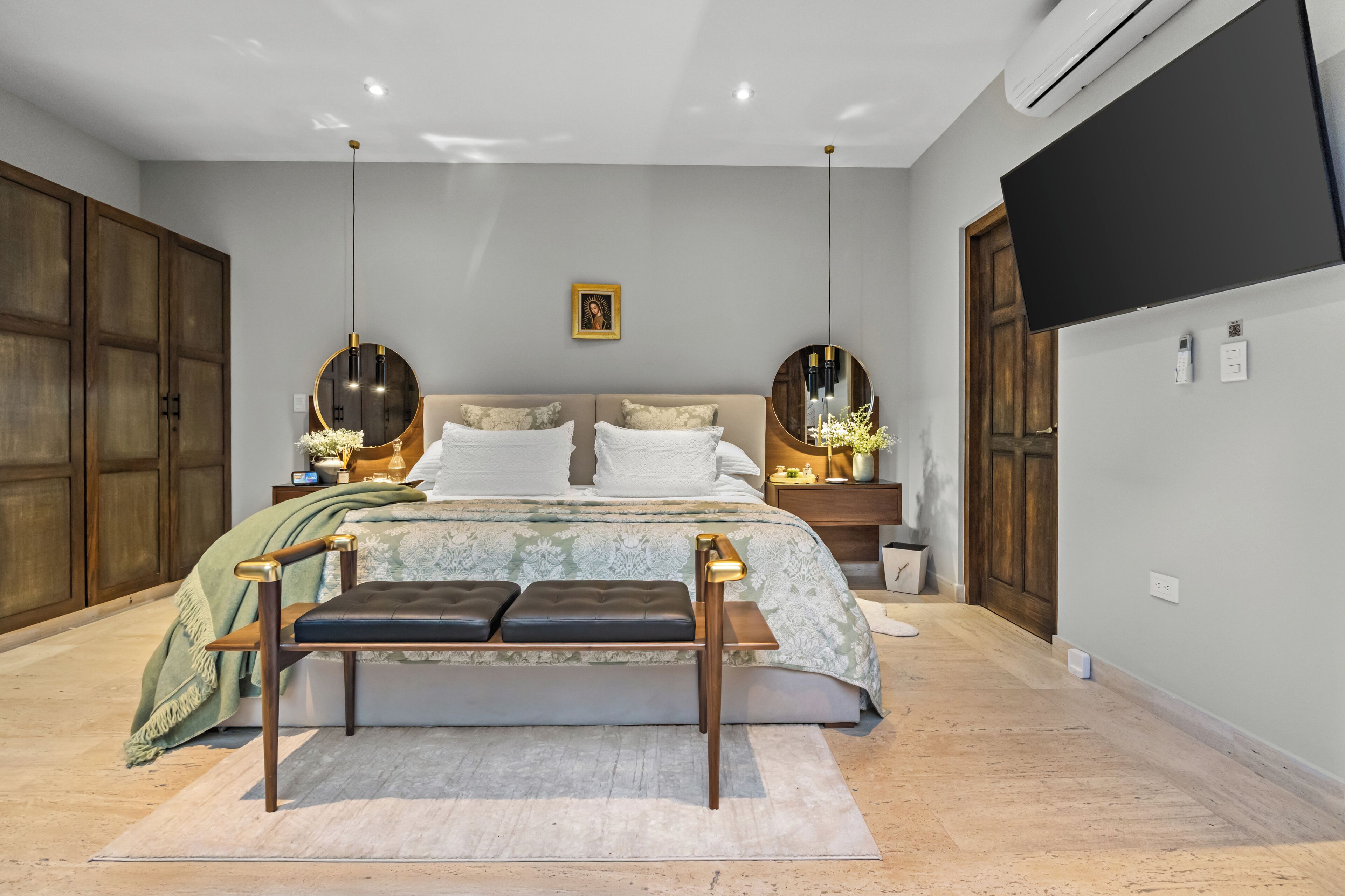 A bedroom with a bed, bedside tables, a bench, a wall-mounted TV, and a door.