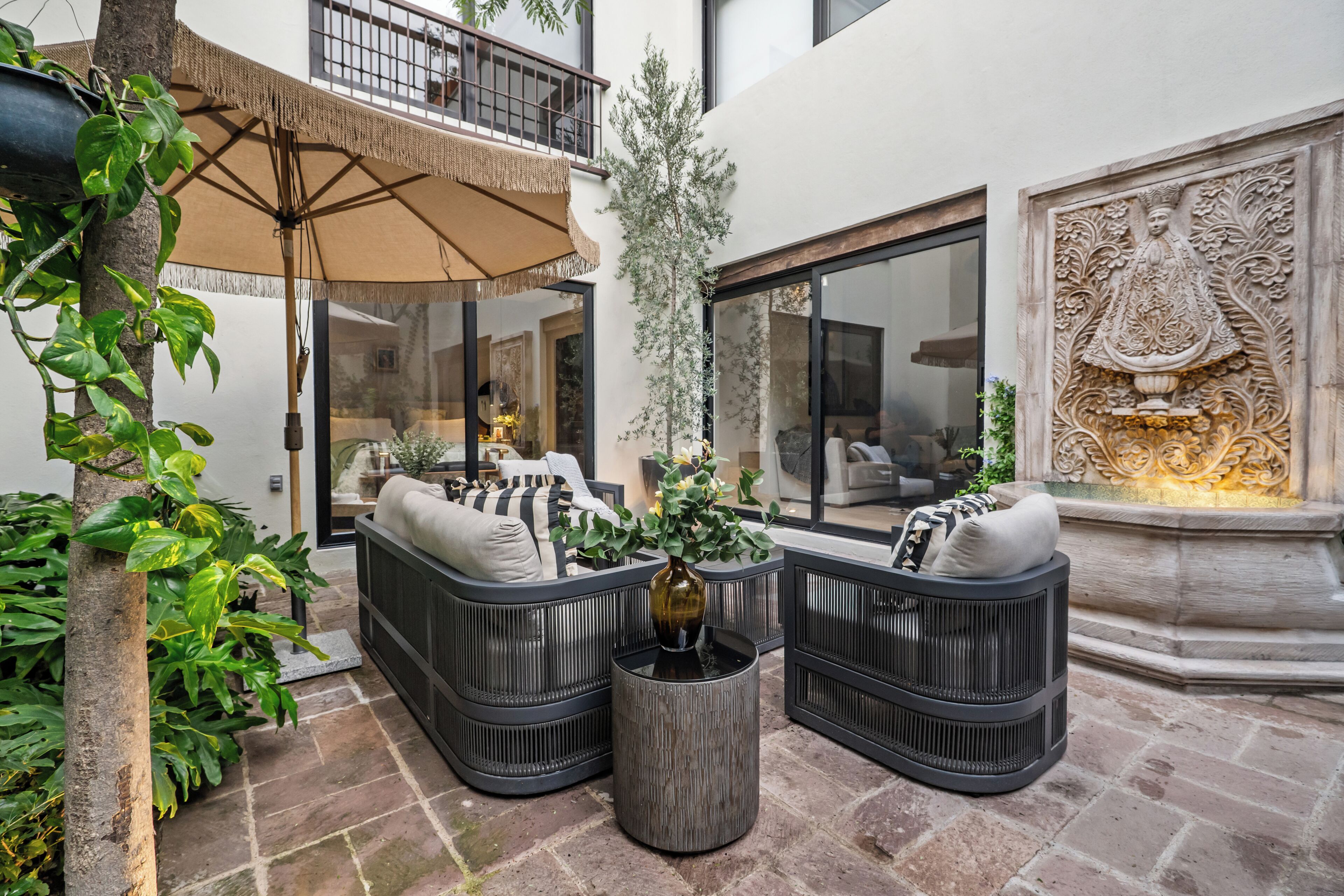 An outdoor seating area with a sofa set, a woven umbrella, and a decorative wall.