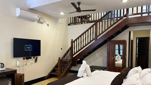 Una habitación de hotel con cama, escritorio, televisión, ventilador de techo y una escalera.