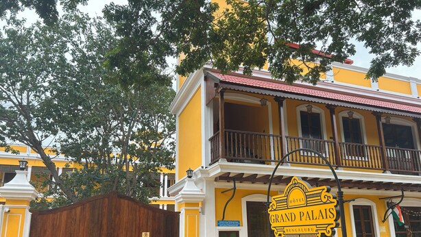 Un edificio amarillo con un letrero que dice 'Grand Palais, Bengaluru' y un letrero de 'Prohibido Estacionar' al frente.