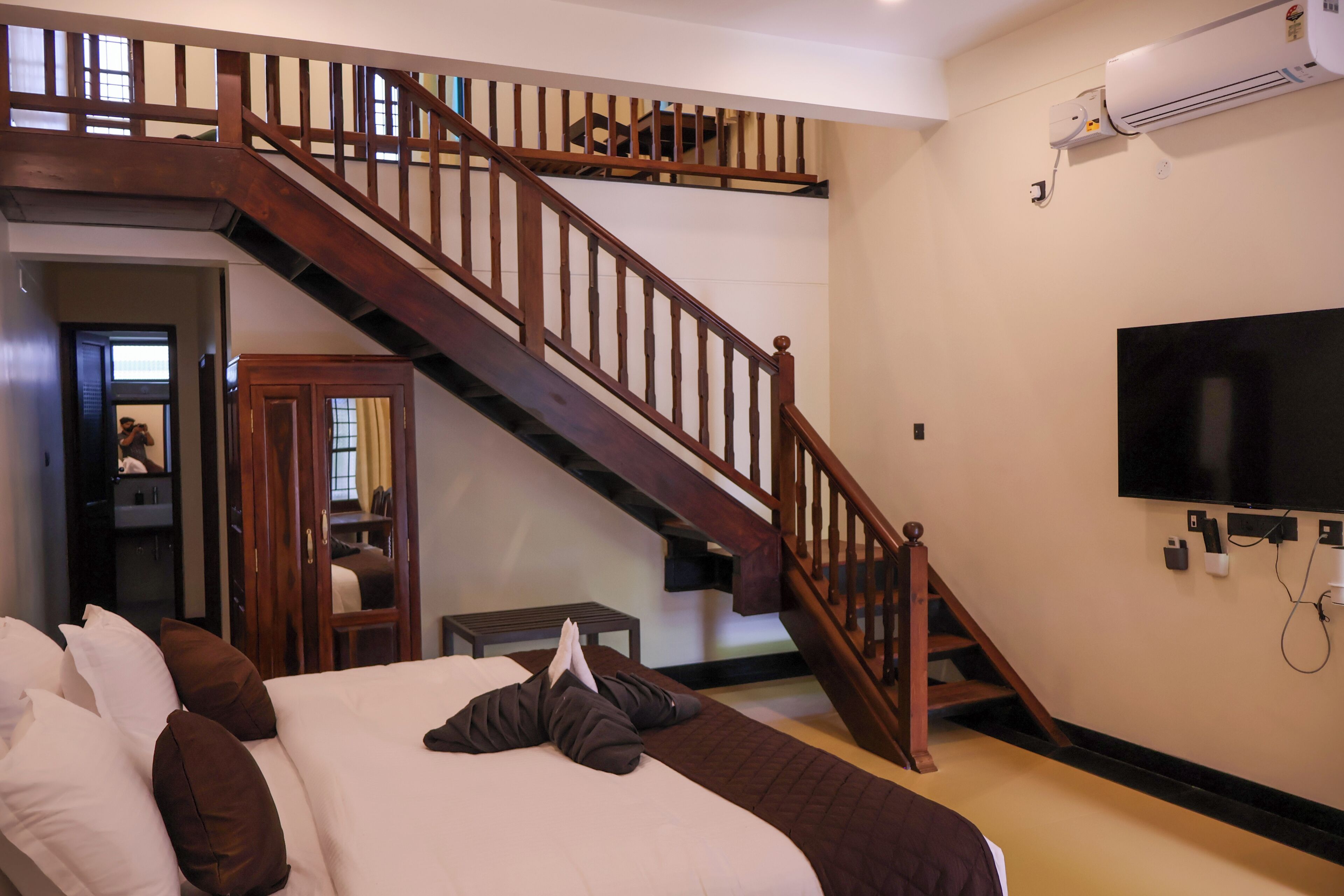 A bedroom with a large bed, a wooden staircase, a television, and an air conditioning unit.