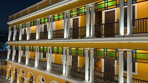 Un hotel de varios pisos con balcones, piso con estampado de cuadros y fachada amarilla.