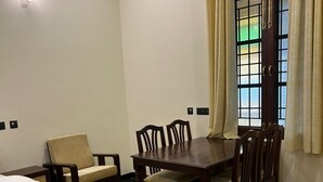 Una habitación de hotel con cama, una mesa de comedor con sillas, un ventanal con cortinas y una lámpara en el techo.