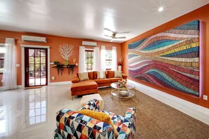 A spacious living room with a large orange sofa, a colorful armchair, and a modern abstract art piece on the wall. - Romantic 2Bed/2Bath/2K - 5★ DT Location -♛Hot Tub (Fort Lauderdale)