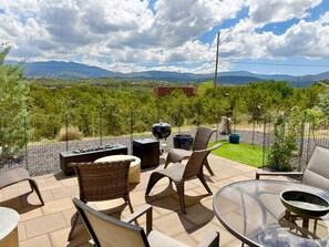 Eine Terrasse im Freien mit Korbmöbeln, einem Glastisch und Blick auf Berge.