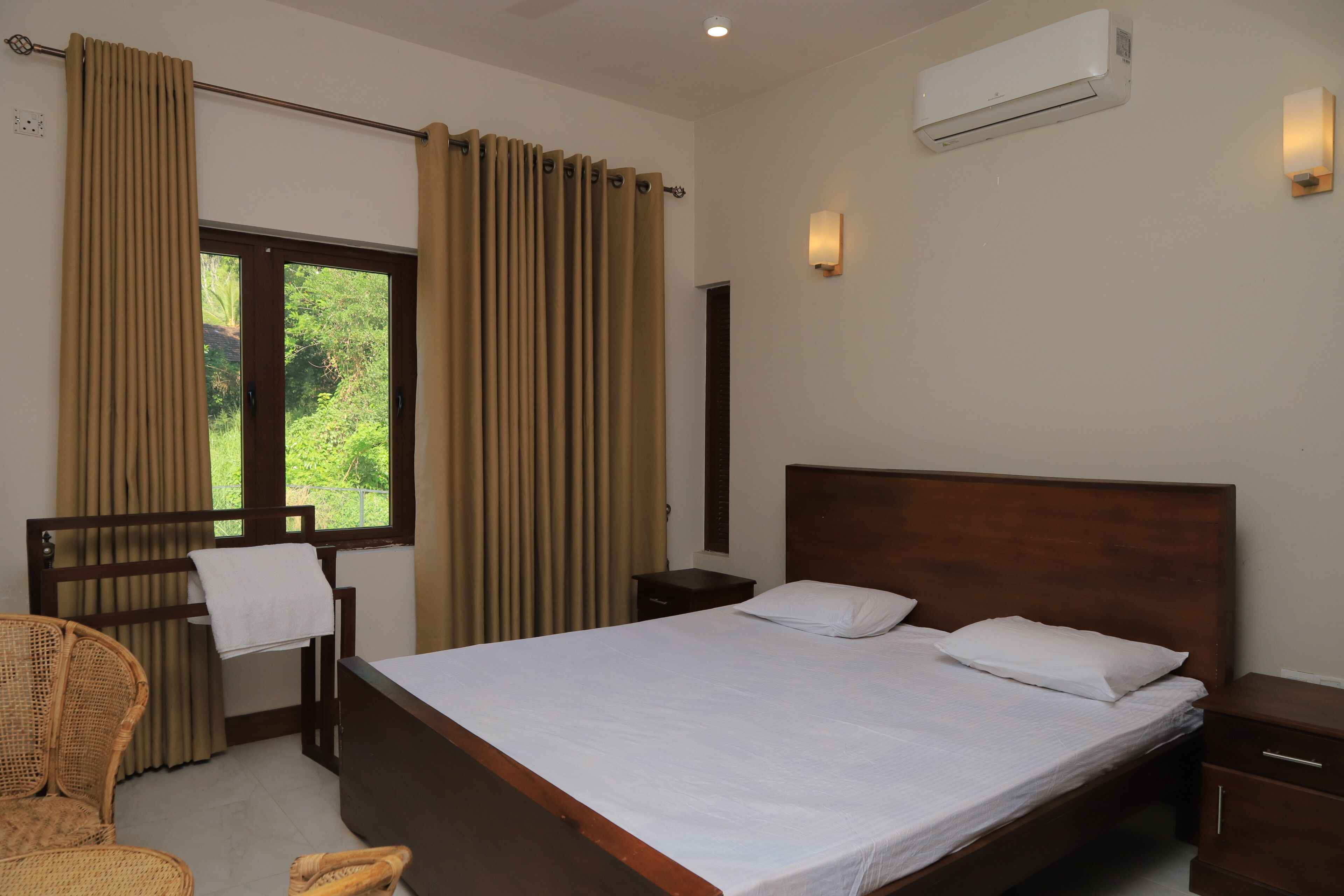 Een hotelkamer met een bed, een stoel, een nachtkastje, een airconditioner en een raam met gordijnen.