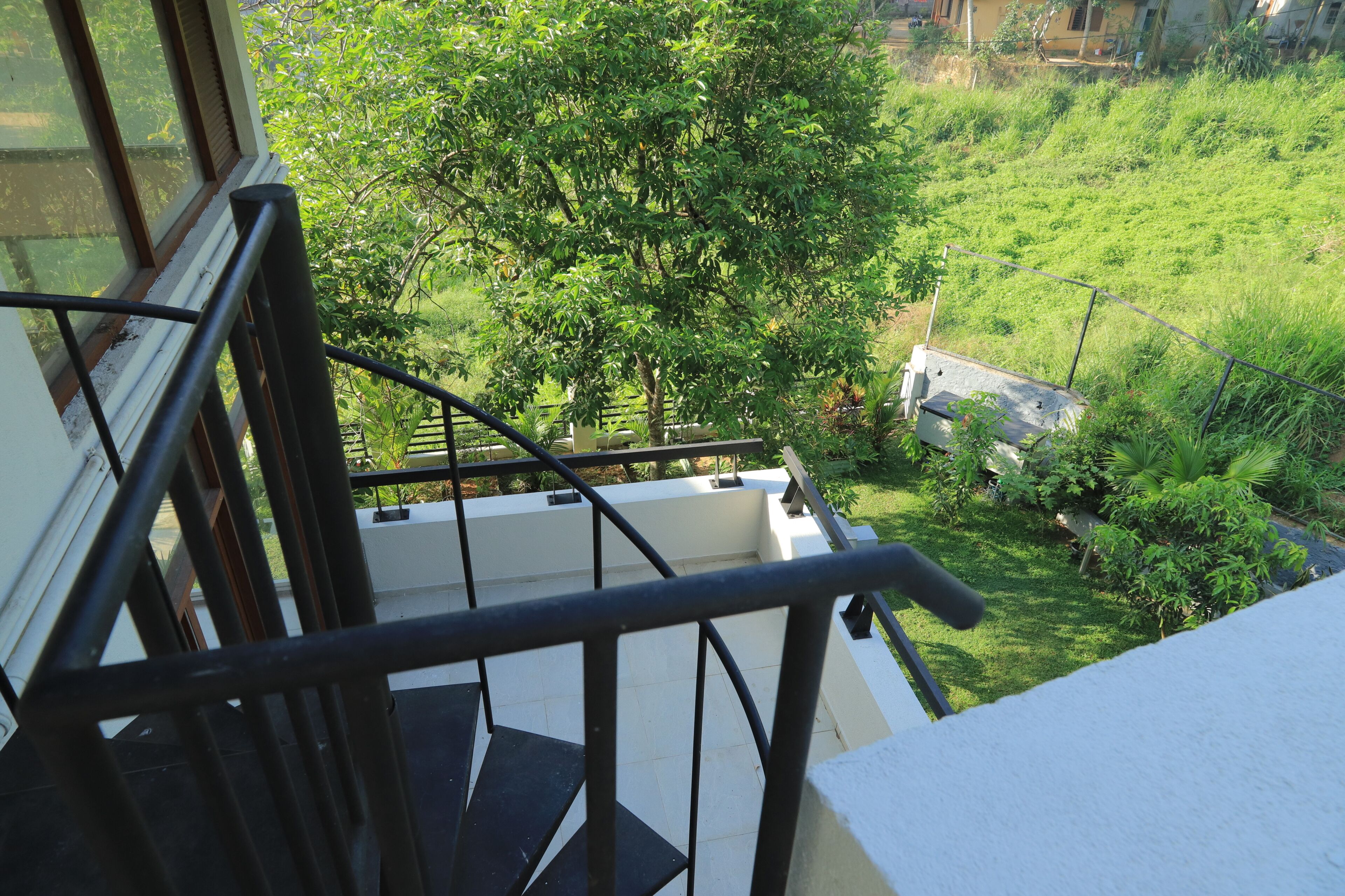 Eine Treppe mit Metallgeländer führt zu einem Balkon mit Blick auf einen üppigen, grünen Garten.