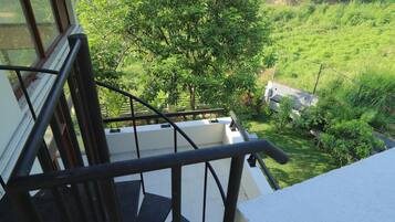 Eine Treppe mit Metallgeländer führt zu einem Balkon mit Blick auf einen üppigen, grünen Garten.