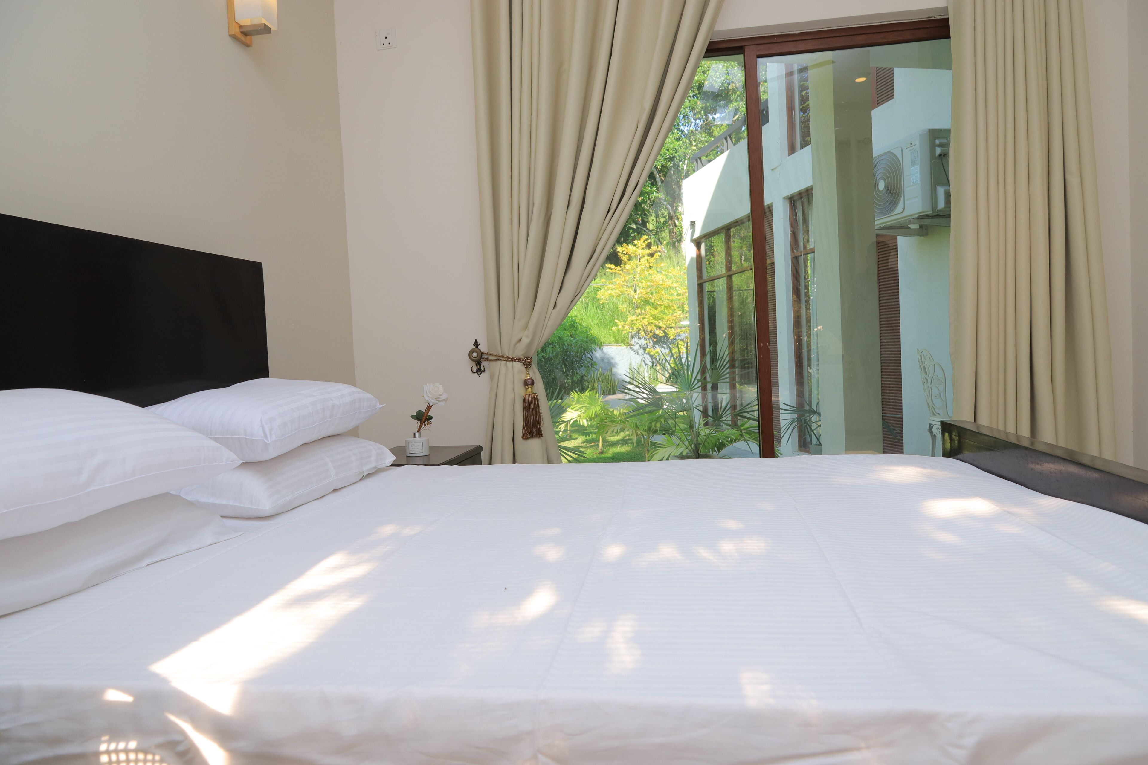 Habitación de hotel con cama, cortinas, mesita de noche y vistas al exterior.
