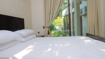 Habitación de hotel con cama, cortinas, mesita de noche y vistas al exterior.
