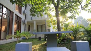 A courtyard with a concrete bench, a small palm tree, and a building with large windows and air conditioning units.