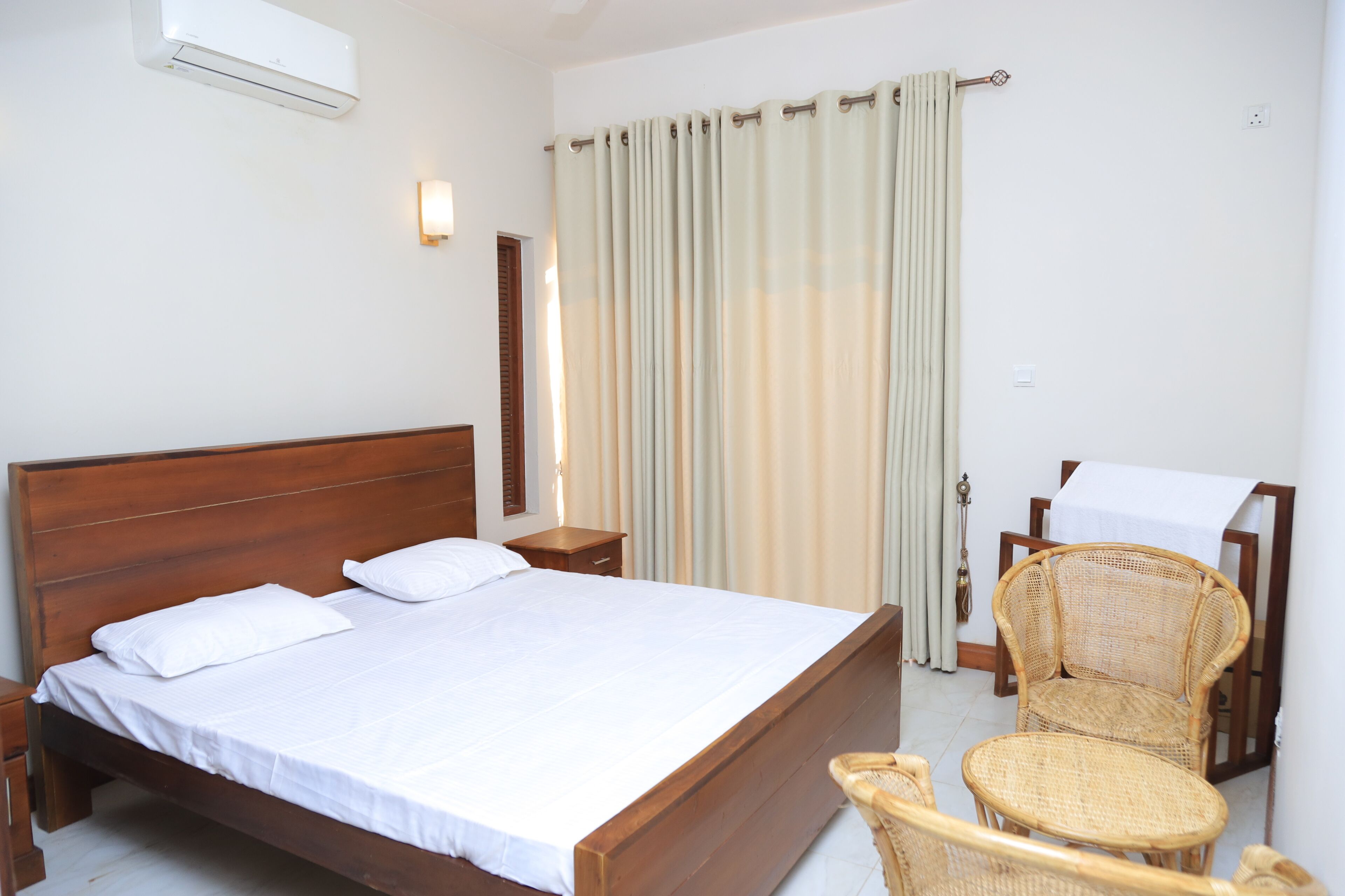 A hotel room with a wooden bed, a bedside table, a chair, and a table with a white tablecloth.