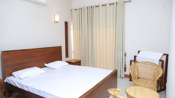 A hotel room with a wooden bed, a bedside table, a chair, and a table with a white tablecloth.