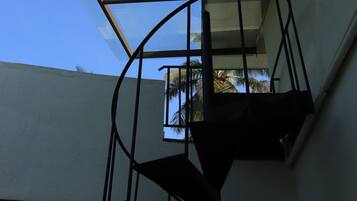 Un escalier en colimaçon doté d’une structure en verre, menant à un balcon d’où l’on peut admirer des palmiers.