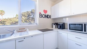 Ett modernt kök med vita skåp, en diskho i rostfritt stål, en mikrovågsugn och ett fönster med utsikt över träd.
