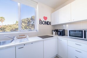 Eine moderne Küche mit weißen Schränken, einer Edelstahl-Spüle, einer Mikrowelle und einem Fenster mit Blick auf Bäume.