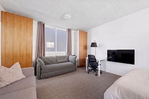 A hotel room with a sofa, a desk, a chair, a TV, and a window with curtains. - Bondi Beach Studio | 2 Min Walk to Beach, Sleeps 4, Work-From-Beach Desk (Bondi Beach)