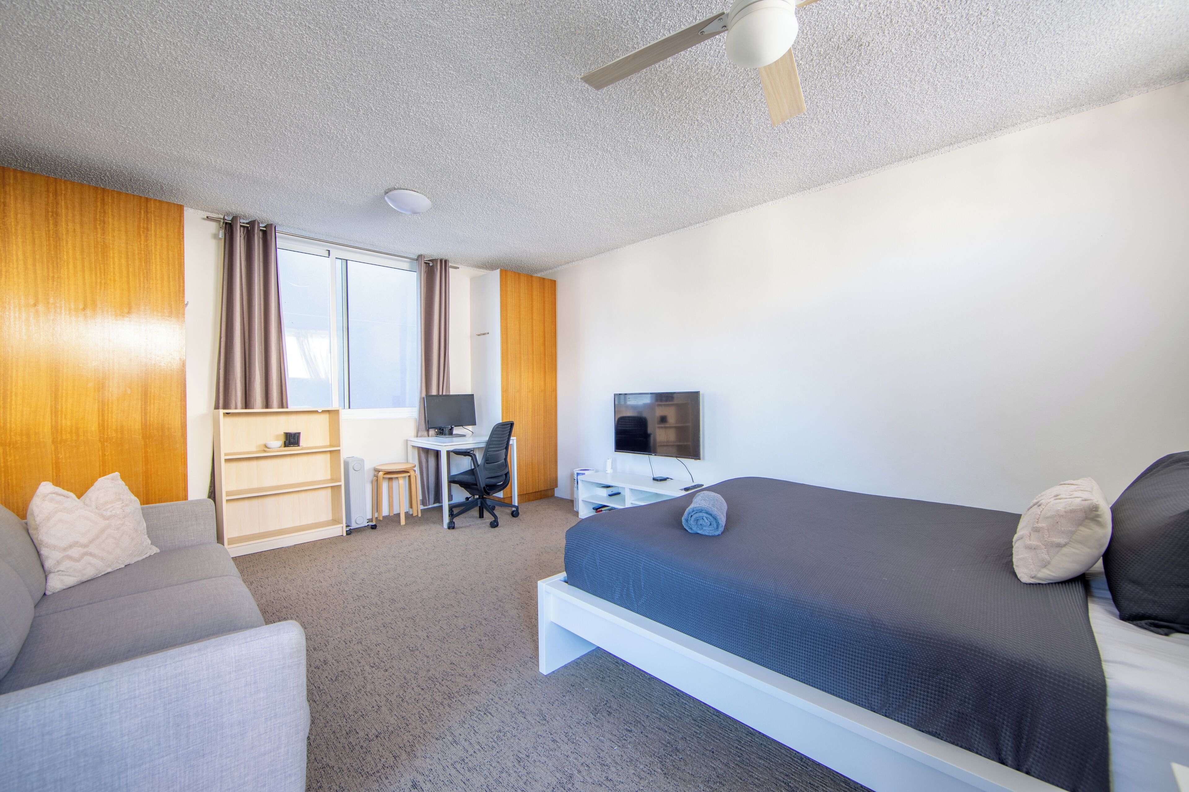 A hotel room with a bed, a desk, a computer, and a television.