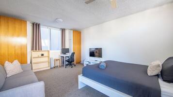A hotel room with a bed, a desk, a computer, and a television.