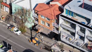 En byggnad med flera våningar, ett rött tak, ett platt tak med solpaneler och en byggarbetsplats med en kran.