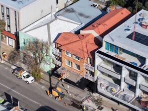Ein mehrstöckiges Gebäude mit rotem Satteldach, einer flachen Dachfläche mit Solaranlage und einer Baustelle mit Kran.